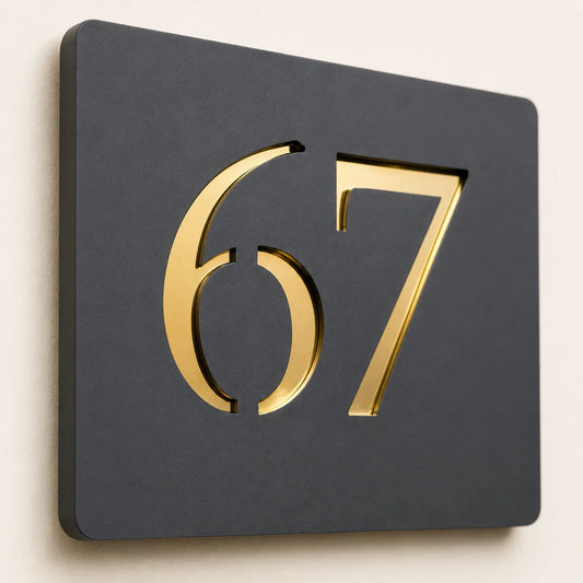 Close-up angled view of a personalised anthracite grey acrylic house sign with raised gold mirror number 67, showcasing the premium layered finish.