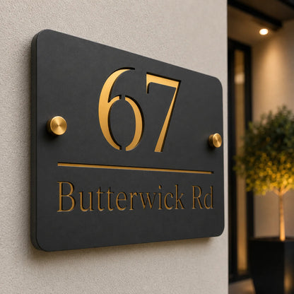Detailed close-up of a modern mineral grey acrylic house sign featuring raised gold mirror number 67, engraved address and premium brass stand-off fixings installed on an exterior wall.