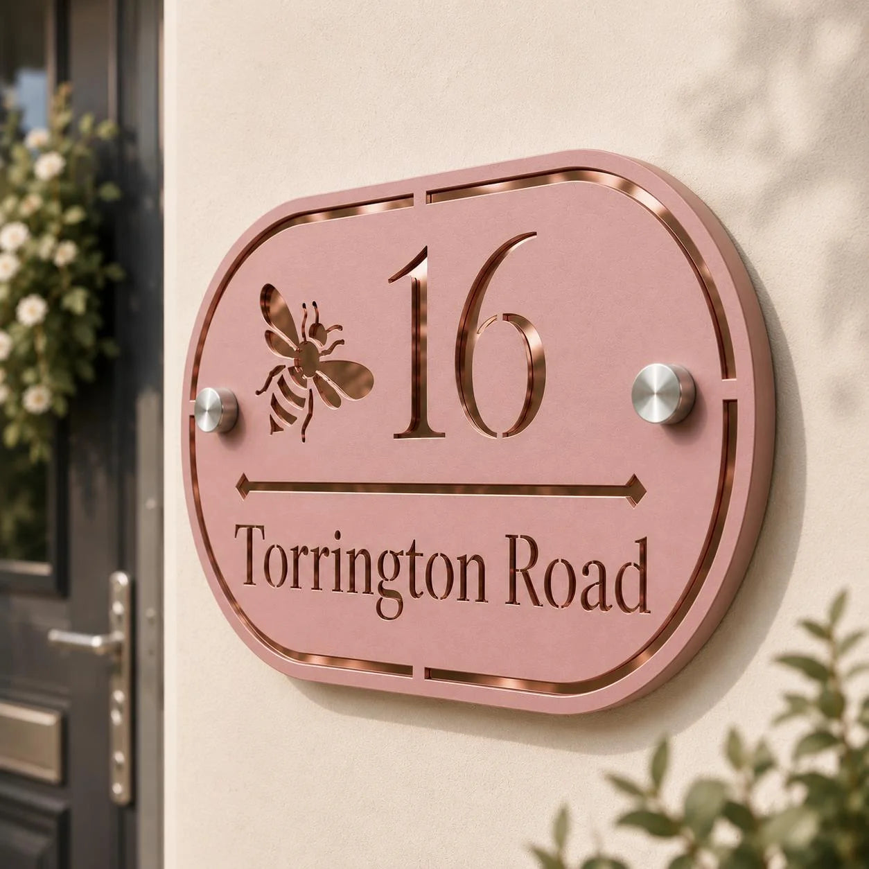 Close-up of personalised dusky pink oval acrylic house sign with mirror rose gold detailing mounted on an exterior wall