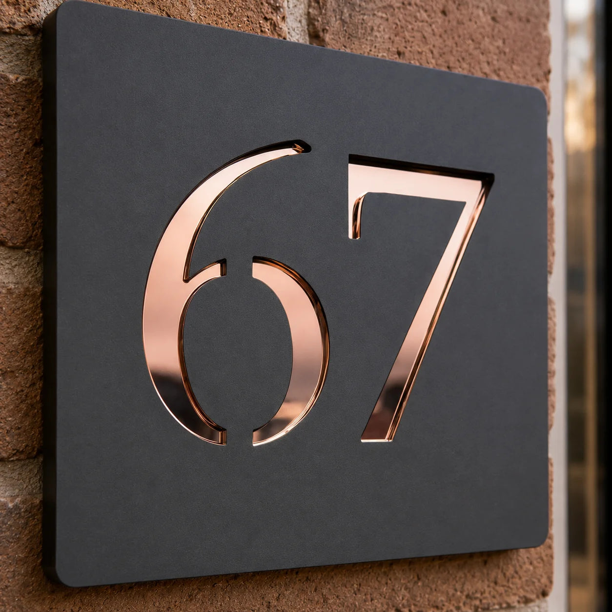 Close-up of a personalised anthracite grey acrylic house sign with raised rose gold mirror numbers mounted beside a modern front door.