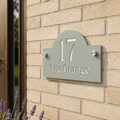 Close-up of personalised sage green arch acrylic house sign mounted on a brick wall beside a front door