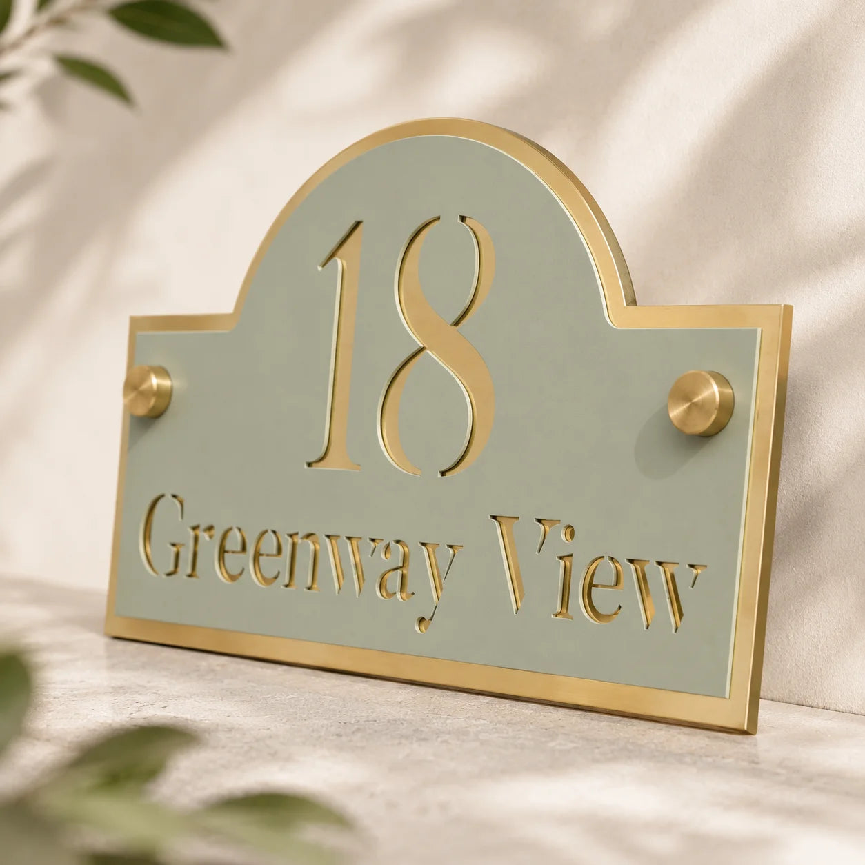 Sage Green and Mirror Gold Arch Acrylic House Sign Close Up blurred leafs in the background 